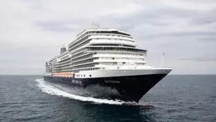 Kreuzfahrtschiff fährt frontal über tiefblaues Meer unter wolkenverhangenem Himmel.