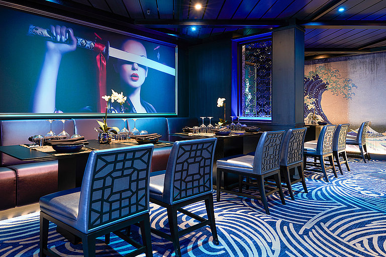 Restaurant mit blau-grauen Akzenten und großem Gemälde auf einem Kreuzfahrtschiff.