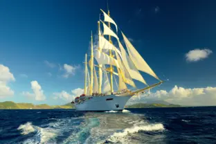 Großes, gold-weißes Segelschiff fährt mit gesetzten Segeln über tiefblaues Meer.