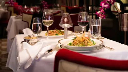 Gedeckter Tisch für zwei Personen mit Weingläsern, Besteck und Teller mit Pasta und Shrimps.