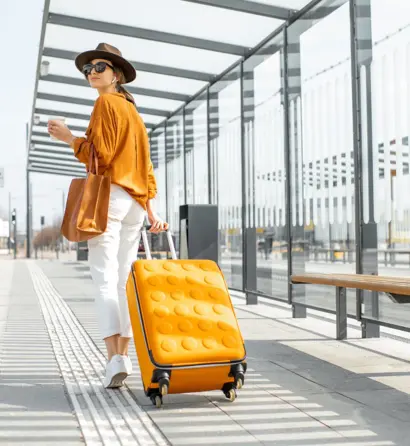 Young female traveler with a luggage at the transport stop Frau mit gelbem Koffer wartet am Flughafen und blickt auf das Rollfeld.