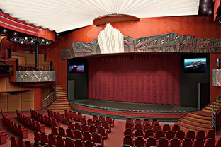 Theater an Bord mit großer Bühne, roten Sitzreihen und festlicher Beleuchtung.