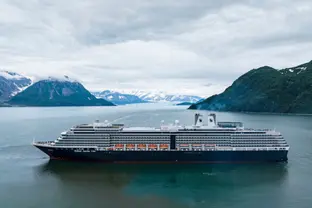 Kreuzfahrtschiff fährt auf dem blauen Wasser mit schneebedeckter Berglandschaft.