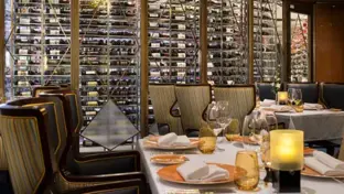 Elegantes Restaurant mit gedeckten Tischen, Kerzenlicht und großer Weinwand im Hintergrund.