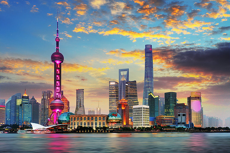 Skyline von Shanghai bei Sonnenuntergang mit Wolkenkratzern und Flussufer.