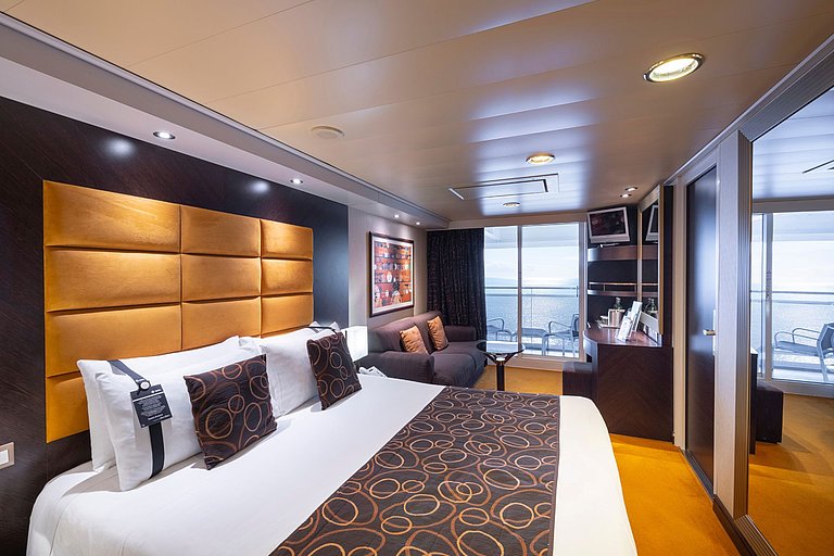 Moderne Schiffskabine mit Doppelbett, Sofa, Balkon, Fernseher und elegantem Wohnbereich.