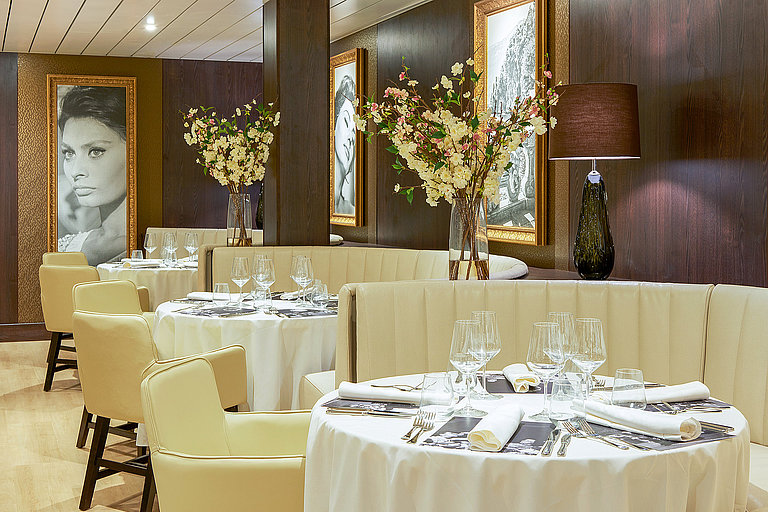 Elegantes Schiffsrestaurant mit gedeckten Tischen, Blumen und warmem Licht.