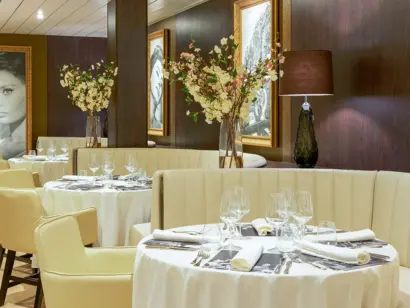 Elegantes Schiffsrestaurant mit gedeckten Tischen, Blumen und warmem Licht.