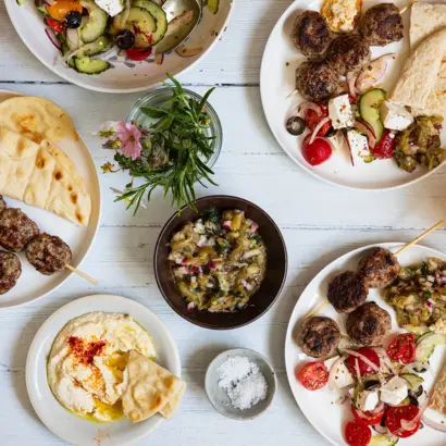 Tisch von oben mit griechischen Speisen, Fladenbrot, Dips, Salt und Oliven.