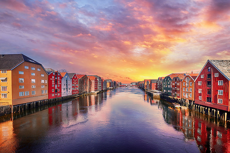Bunte Speicherhäuser am Wasser in Trondheim bei leuchtendem Sonnenuntergang.