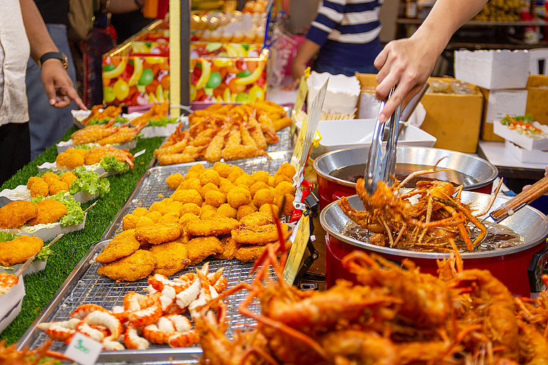 Streetfood-Stand mit frittierten Snacks, Spießen und bunten Speisen auf dem Markt.