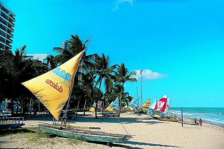 Sandstrand in Brasilien mit reichlich Besuchern, Palmen, Wolken und blauem Meerwasser.