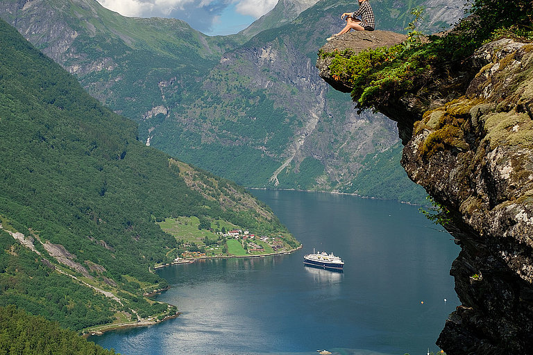 Blick auf Fjord und Dorf zwischen steilen grünen Bergen in Norwegen.