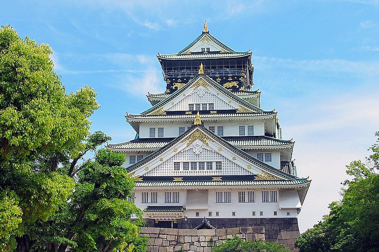 Weißes Schloss Himeji mit geschwungenen Dächern, umgeben von grünen Bäumen.