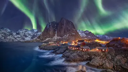 Nordlichter über verschneitem Fischerdorf, Bergen und Küste auf den Lofoten.