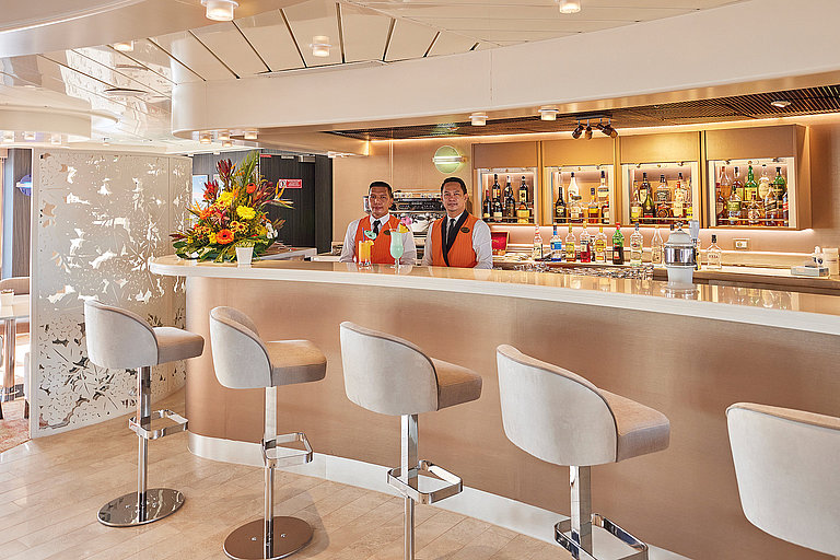 Helle Bar an Bord eines Kreuzfahrtschiffs mit Theke, Hockern und Regalen.