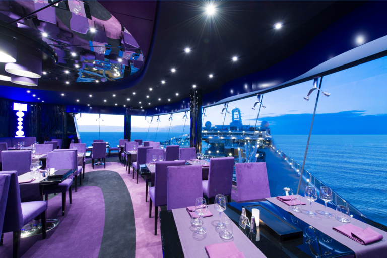 Elegantes Schiffsrestaurant mit violettem Licht, Panoramafenstern und blauem Meerblick.