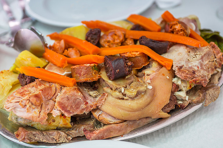 Nahaufnahme eines traditionellen Gerichts der Azoren auf einem Teller, mit Fleisch und Gemüse.
