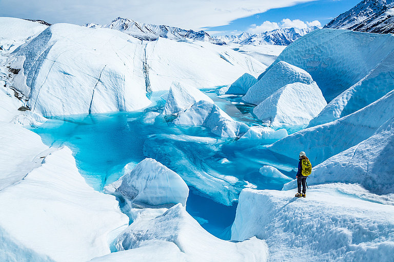 Person zwischen blauen Eisformationen in weiter Gletscherlandschaft mit Schnee.
