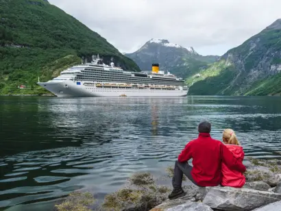 Paar in roter Kleidung bestaunt ein vorbeifahrendes Kreuzfahrtschiff im Tal.