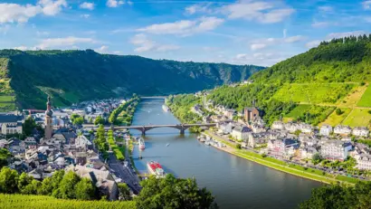 Panoramablick auf Fluss, Stadt und grüne Hügel unter bewölktem Himmel.