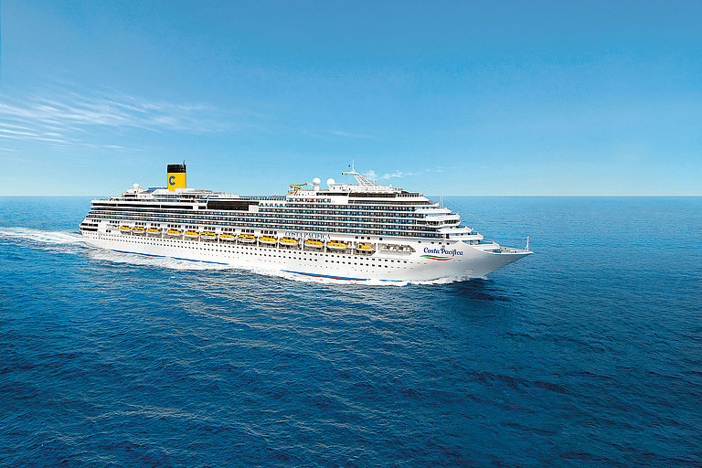 Weißes Kreuzfahrtschiff mit Schiffsschornstein fährt über tiefblaues Meer unter leicht bewölktem Himmel.