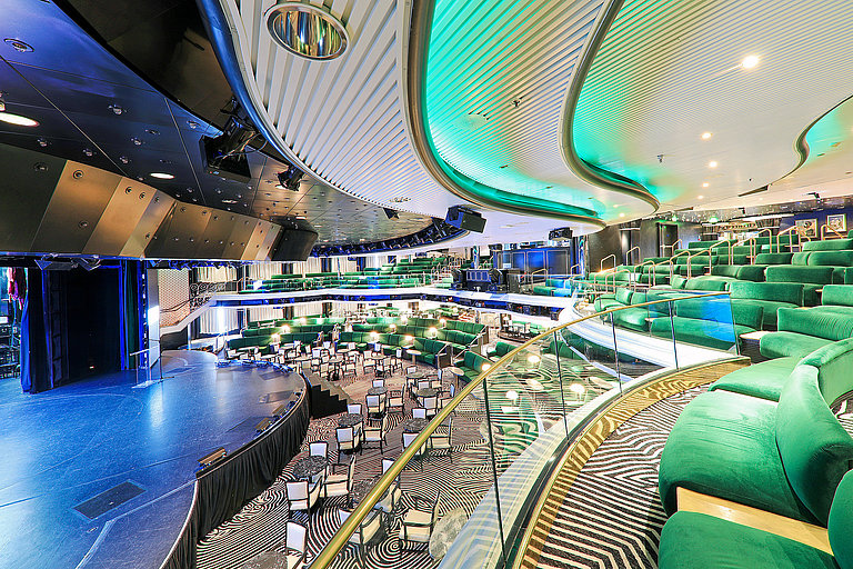 Großes Schiffstheater mit Bühne, grünen Sitzreihen und geschwungener Lichtdecke.