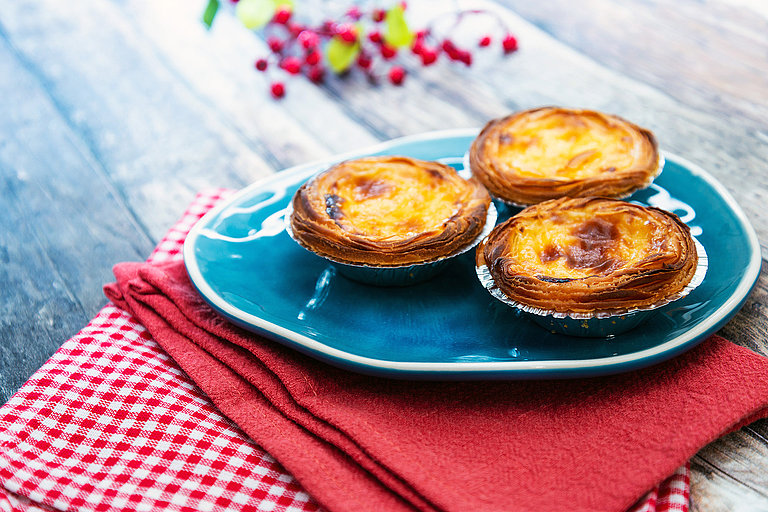 Pastéis de Nata auf blauem Teller mit roter Serviette und Holztisch.