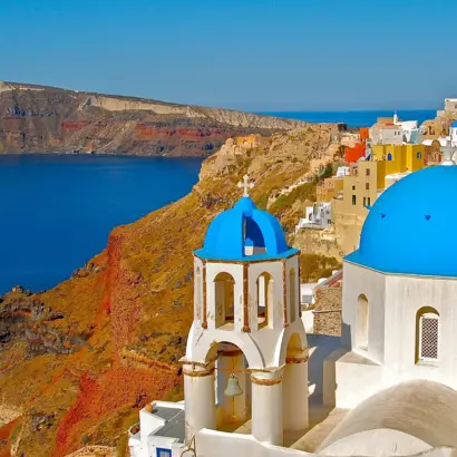 Weiße Häuser mit blauen Kuppeln an der Küste von Santorin über tiefblauem Meer.