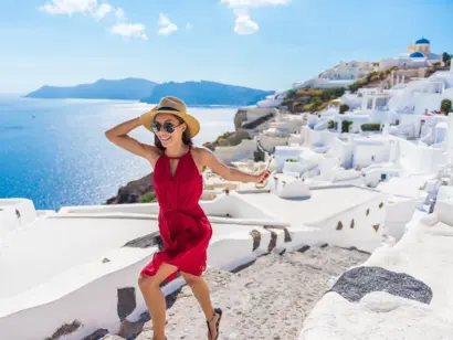 Frau im roten Kleid vor weißen Häusern mit Blick über Santorin und das Meer.