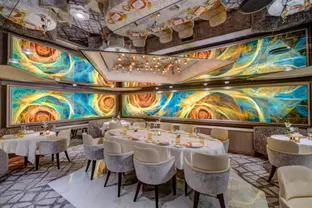Elegantes Restaurant an Bord mit kunstvoller Wandgestaltung, Deckenspiegeln und gedeckten Tischen.