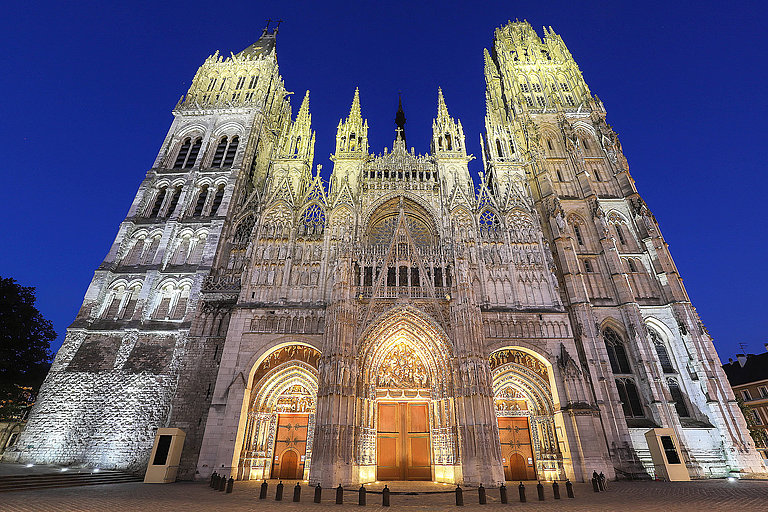 Festlich beleuchtete Kathedrale mit gotischer Fassade vor tiefblauem Nachthimmel.