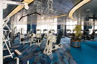 Fitnessbereich mit verschiedenen Fitnessgeräten und großen Fenstern mit Blick aufs Meer.