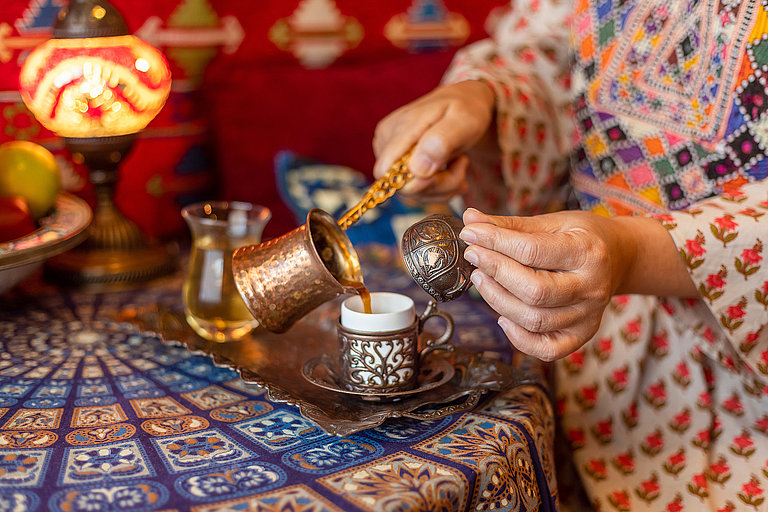 Traditionelle Kaffeezubereitung mit Kupferkännchen auf bunt gemustertem Tuch.