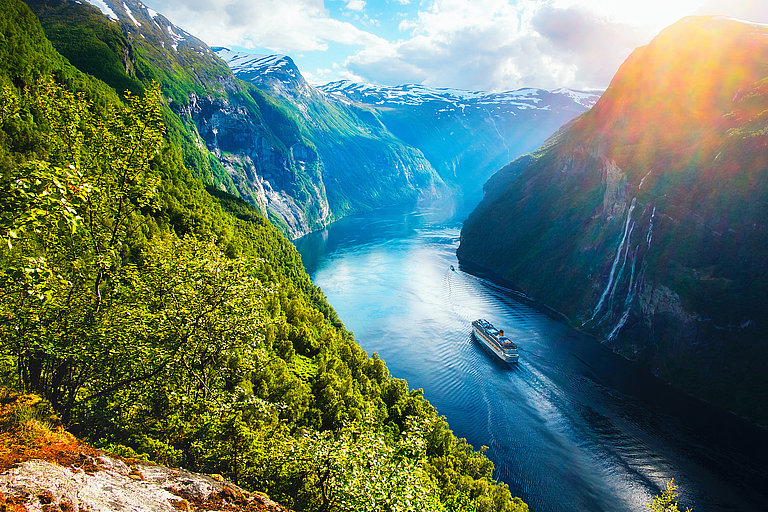 Norwegische Fjorde sind berühmt für ihrs tiefblauen, glazialen Meeresarme, die von majestätischen, steil aufragenden Bergen und malerischen Wasserfällen umgeben sind.