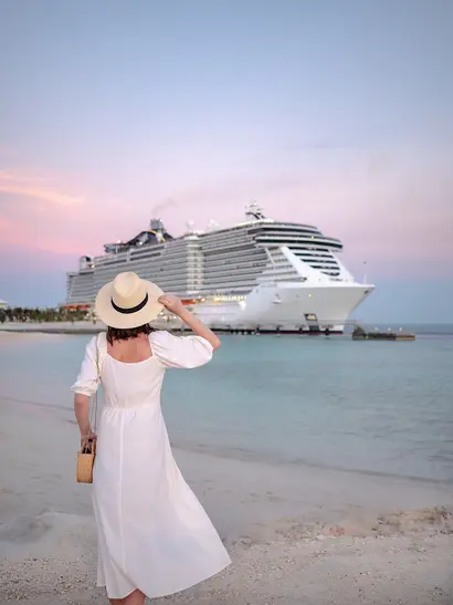 Young woman by the cruise ship at sunset Das Bild zeigt eine Frau, die an einem Strand steht und ein großes Kreuzfahrtschiff betrachtet.