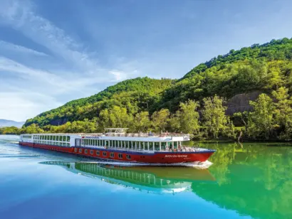 Weiß-rotes Flusskreuzfahrtschiff auf türkisblauem Wasser, vor dicht bewaldetem grünen Ufer.