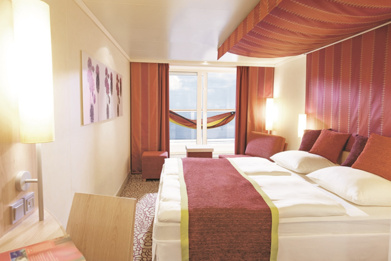 Blick in eine Balkonkabine mit Doppelbett, mit Blick auf das Wasser.