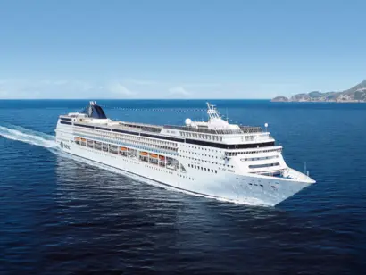 Weißes Kreuzfahrtschiff auf weitem Ozean mit kleiner Küste rechts im Hintergrund.