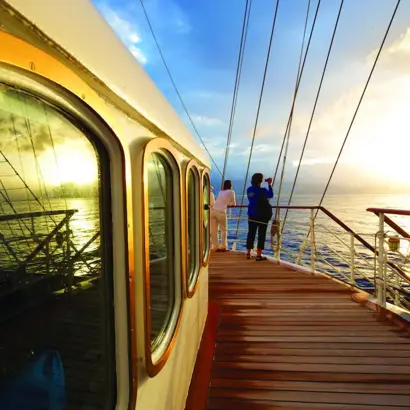 Paar steht auf dem Deck eines Segelschiffes mit Blick auf das blaue Meer.