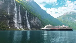 Kreuzfahrtschiff im grünen Fjord vor steilen Felswänden und hohen Wasserfällen.