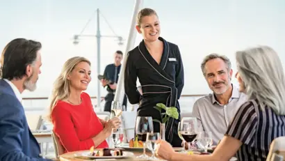 Zwei Paare am Esstisch mit Weingläsern bestellen ihr Essen, mit Blick auf das Meerwasser.