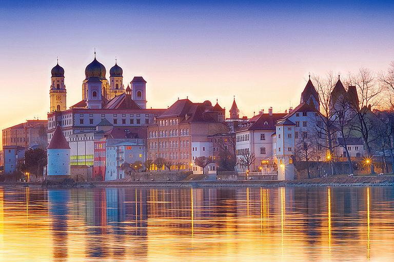 Historische Uferstadt mit Kirchenkuppeln, im Abendlicht golden im Wasser gespiegelt.