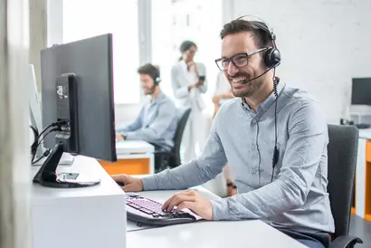 Junger Mann mit Headset arbeitet im Callcenter am Computer neben seinen Kollegen.