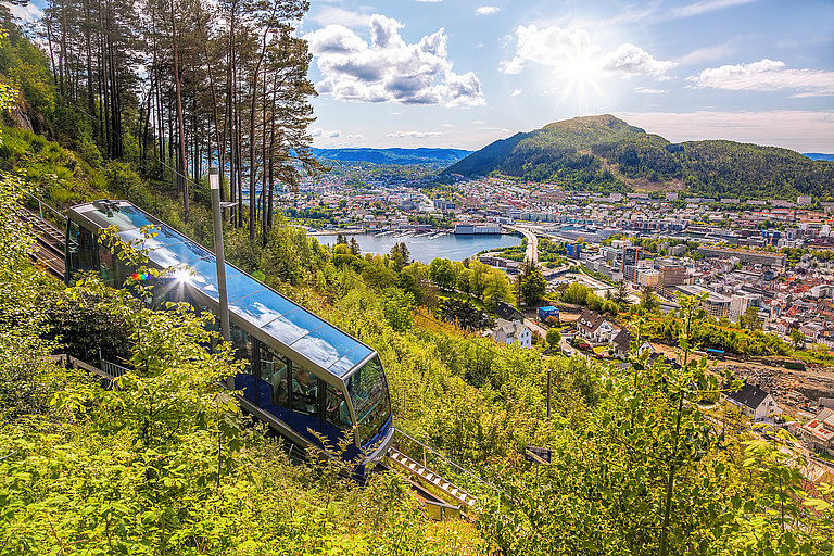 Standseilbahn über Bergen mit Blick auf Stadt, Fjord und grüne Berge im Sonnenschein.