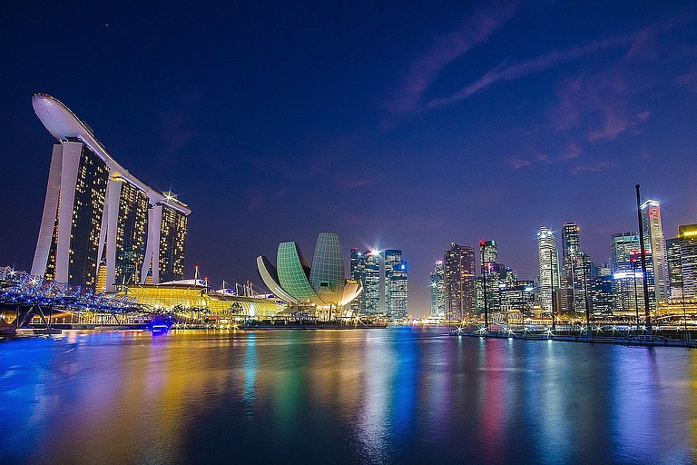 Beleuchtete Skyline bei Nacht, gespiegelt im Wasser vor dunklem Himmel.