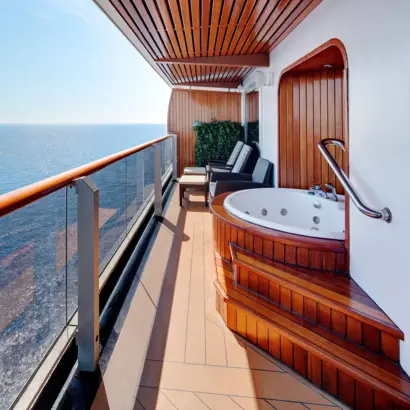 Balkon eines Kreuzfahrtschiffes mit Whirlpool, Holzelementen und Blick aufs Meerwasser.
