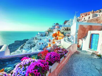 Gasse mit weißen Häusern, bunten Blumen und Blick auf das Meer in Santorin.
