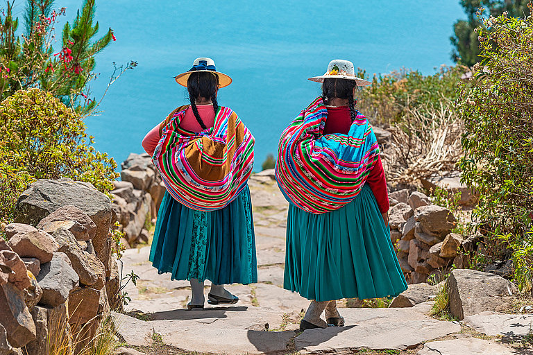 Zwei Frauen in traditioneller Kleidung stehen auf einer Steintreppe in Peru.