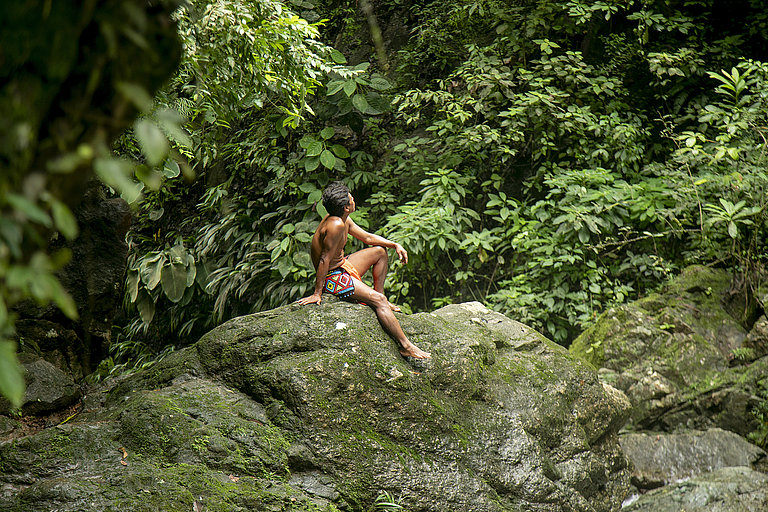 Person springt im dichten Regenwald zwischen grünen Felsen und Pflanzen.
